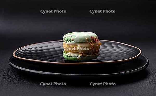 Food, Beautiful tasty macaron with filling and fruit flavor on a black plate on a dark concrete background [IBR124876426]