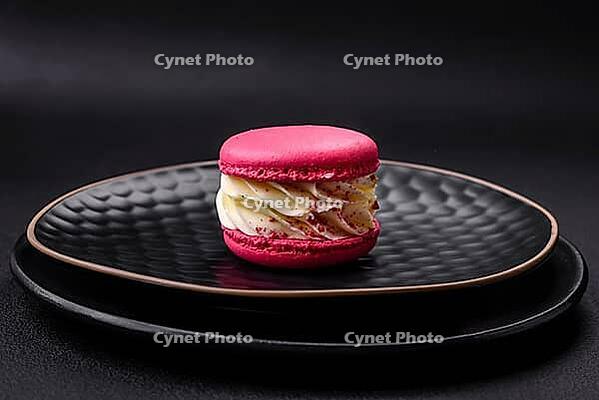 Food, Beautiful tasty macaron with filling and fruit flavor on a black plate on a dark concrete background [IBR124876442]