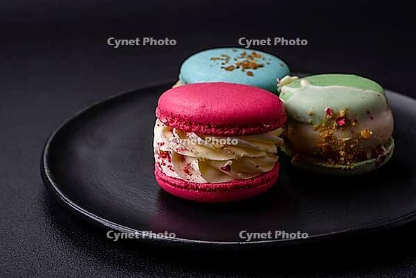 Food, Beautiful tasty macaron with filling and fruit flavor on a black plate on a dark concrete background [IBR124876443]