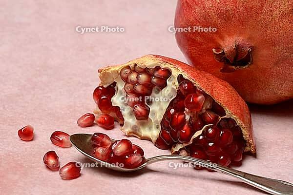 Opened pomegranate and pomegranate seeds in a spoon, Punica granatum [IBR124899848]