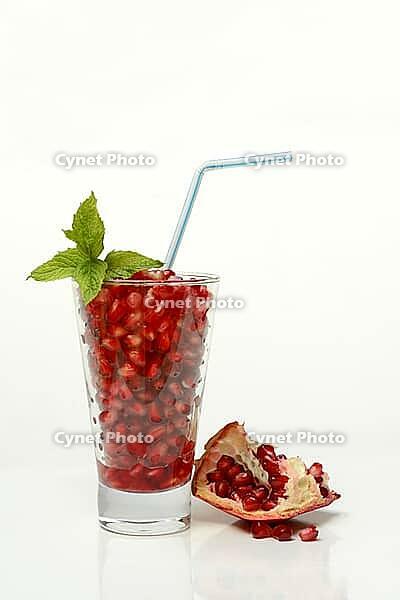 Pomegranate seeds in glass and straw, halved pomegranate [IBR124899853]