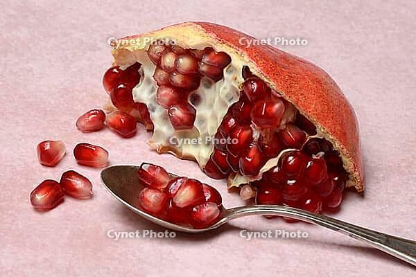 Opened pomegranate and pomegranate seeds in a spoon, Punica granatum [IBR124899866]