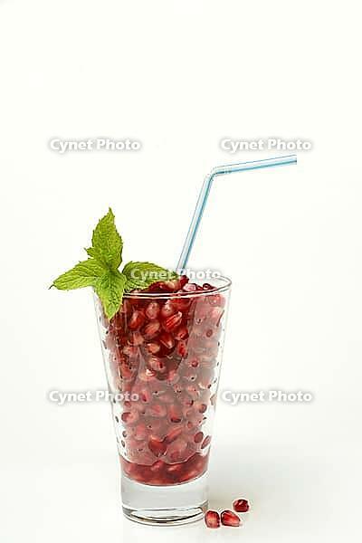 Pomegranate seeds in glass and straw, halved pomegranate [IBR124899867]