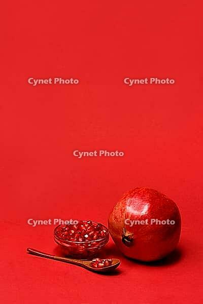 Pomegranate and seeds in wooden spoon and bowl, with red background, Punica granatum [IBR124899869]
