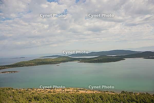 A tranquil panorama of Ayvalık's emerald islands and calm waters unfolds beneath soft, drifting clouds [IBR124899886]
