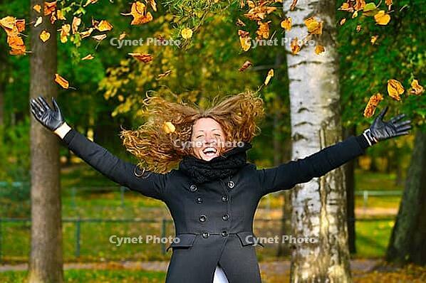 Happy woman is throwing dry autumn leaves in park [IBR124906358]