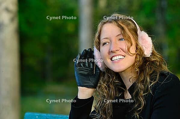 Young woman is sitting on the bench in autumn park and listening [IBR124906360]