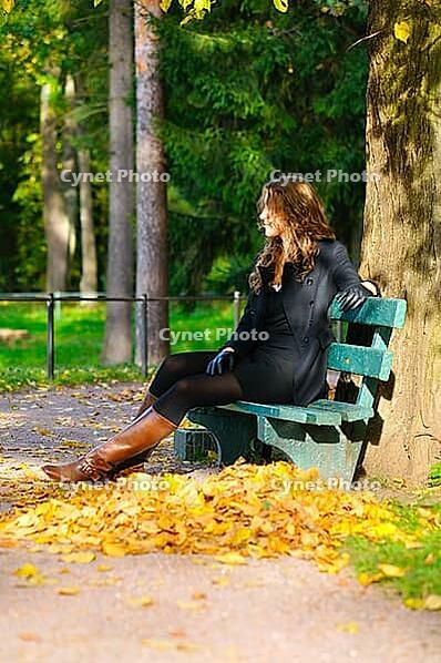 Young woman is sitting on the bench in autumn park and looking sideways [IBR124906361]