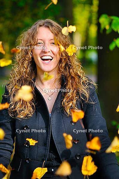 Happy woman is throwing dry autumn leaves in park [IBR124906364]