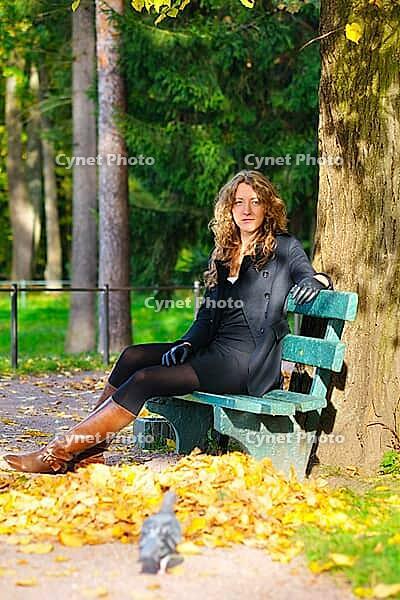 Young woman is sitting on the bench in autumn park and looking at camera [IBR124906366]