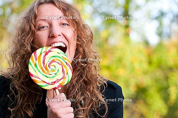 Happy woman is eating a big lollipop in park [IBR124906384]