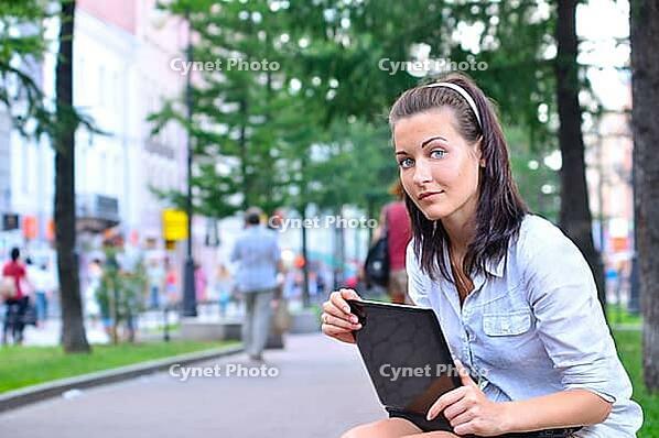 Beautiful woman is sitting in city with laptop and looking at camera [IBR124906396]
