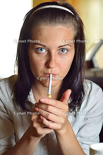 Young woman is lighting a cigarette in a cafe [IBR124906401]