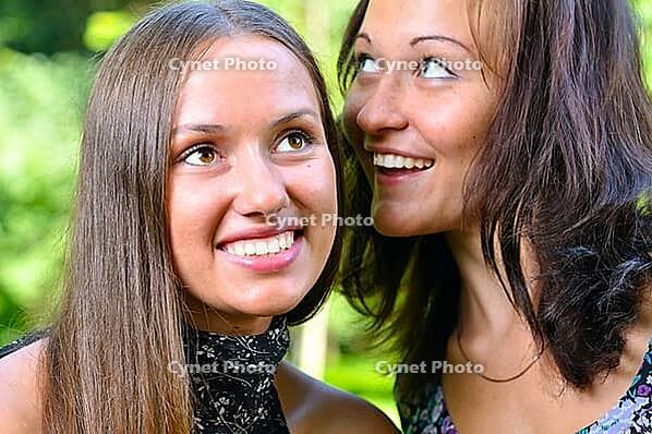 Two female friends are sharing secrets in summer park [IBR124906402]
