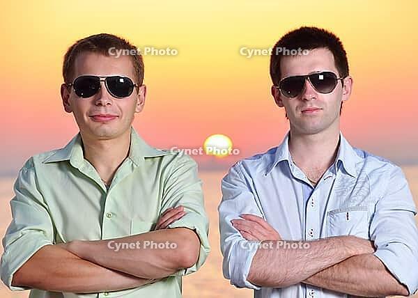 Two friends at sunset wearing sunglasses fold their arms [IBR124906407]