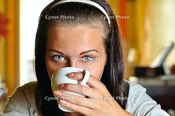 Young woman is drinking coffee in cafe and looking at camera [IBR124906416]