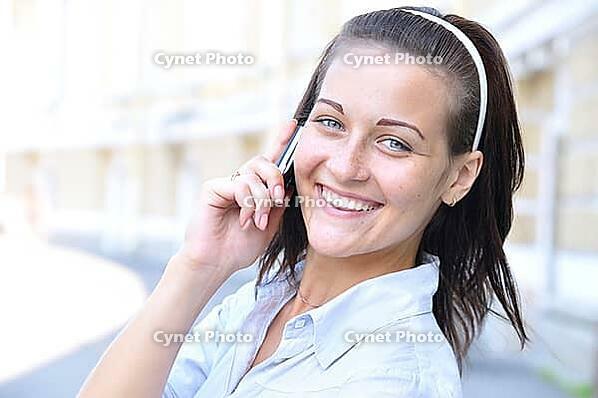 Beautiful smiling woman is talking phone at sunny street [IBR124906422]