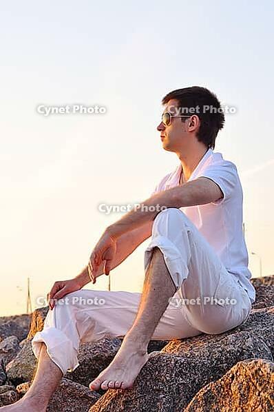 Man is sitting on stones at sunrise [IBR124906425]