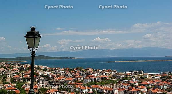 A picturesque seaside town with terracotta rooftops gazes toward tranquil blue waters and distant islands [IBR124920188]