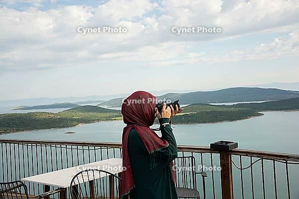 Traveler captures peaceful coastal panorama from terrace overlooking blue water and green islands [IBR124920204]