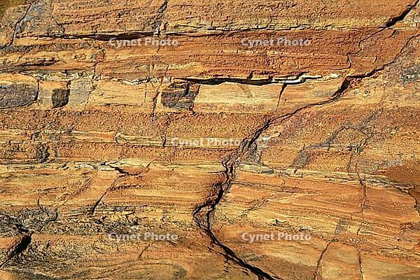 Detailed nature photo of a reddish-brown sandstone formation on a coast. The close-up shows the distinctive texture of horizontal sediment layers formed by centuries of erosion. Embedded in the rocky structure are various smaller, colorful pebbles and tid [IBR124920208]