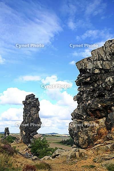 Spectacular view of the historic Devil's Wall in an idyllic heath landscape. The mighty sandstone rock formation fascinates with its rugged structures, earthy tones and a distinctive, free-standing rock needle in the background. A wooden rope fence lines  [IBR124920217]