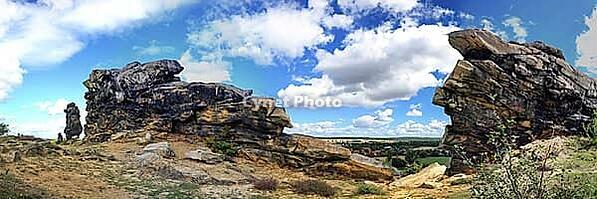 Spectacular view of the historic Devil's Wall in an idyllic heath landscape. The mighty sandstone rock formation fascinates with its rugged structures, earthy tones and a distinctive, free-standing rock needle in the background. A wooden rope fence lines  [IBR124920219]