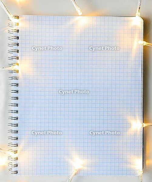 Christmas lights on gray table with notebook, view from above [IBR124944034]