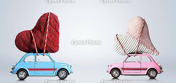 Couple of retro toy cars delivering craft hearts for Valentine's day on gray background [IBR124944051]