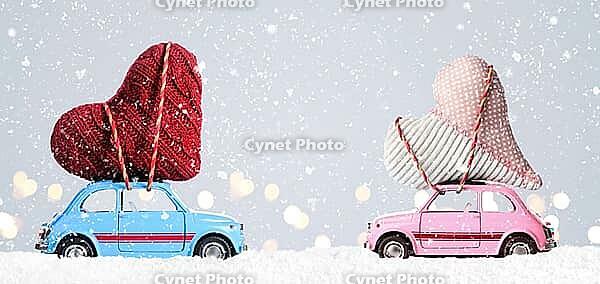 Couple of retro toy cars delivering craft hearts for Valentine's day on gray background with flying cars [IBR124944052]