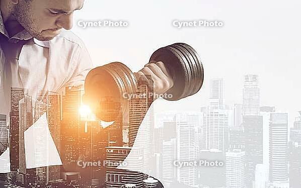 Hard working business concept. Strong businessman with dumbbell mixed with sunset city skyline [IBR124944116]