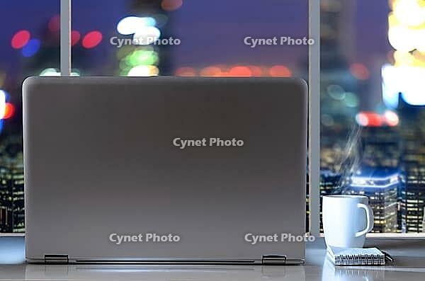 Laptop on table in office with panoramic night view of modern downtown skyscrapers at business district [IBR124944125]