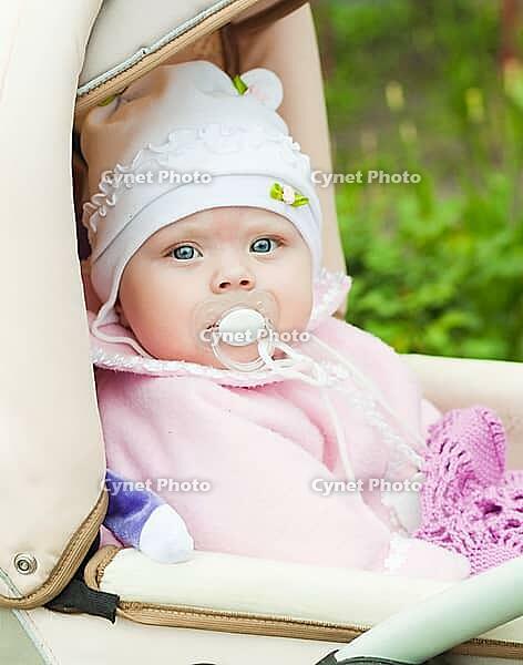 Little girl of seven months in the pushchair sits in the park [IBR124991082]