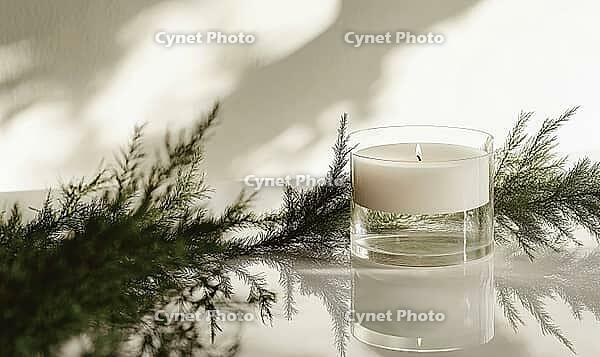 Minimalist candle arrangement with a single white candle in a transparent holder, surrounded by green fir branches. AI generated [IBR125000267]