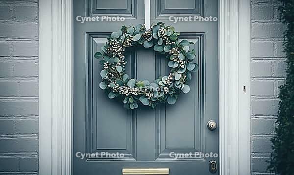 Simple holiday wreath made of pine branches and small white berries, hanging on a light gray wall. AI generated [IBR125000288]