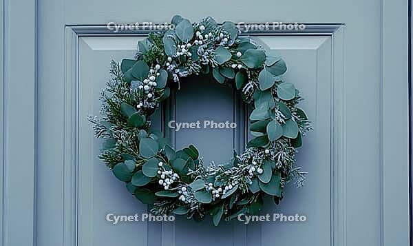 Simple holiday wreath made of pine branches and small white berries, hanging on a light gray wall. AI generated [IBR125000289]