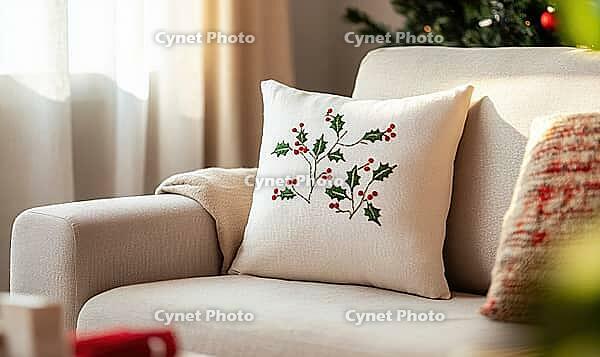 White linen pillow with red and green holly embroidery, set against a beige sofa in a minimalist living room. AI generated [IBR125000308]