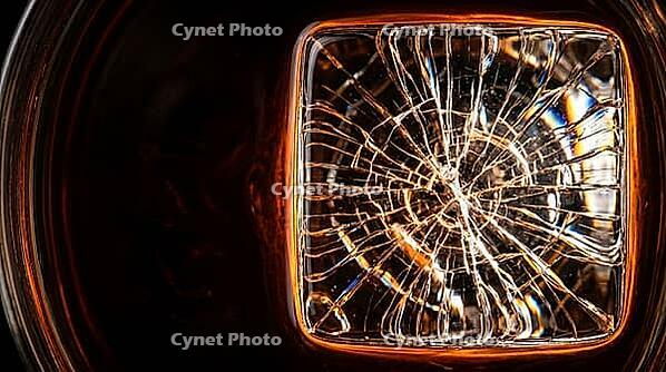 Ultra-extreme macro close-up of single large clear craft ice cube submerged in dark rum inside rocks glass showing thermal fracture hairline cracks radiating from centre caught by single Dedolight spot transmitting through ice into prismatic light threads [IBR125000323]
