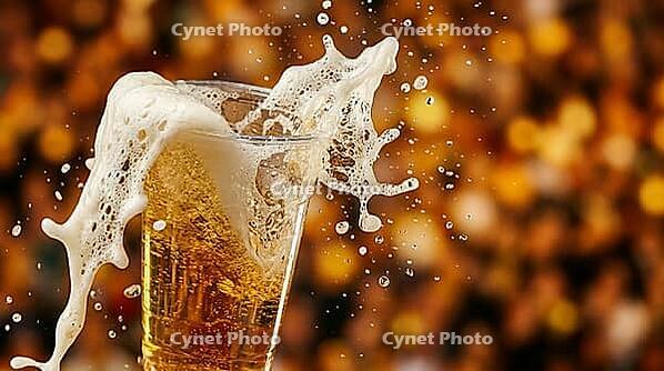 Extreme macro close-up of clear plastic stadium cup of golden beer with foam violently overflowing rim in multiple directions simultaneously from sudden movement, dense white-cream foam cascade mid-fall over left edge with individual beer droplets airborn [IBR125000334]
