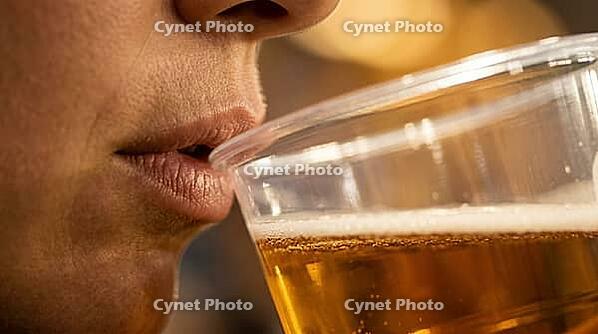 Extreme macro close-up of anonymous human lips only visible from nose base to chin at precise moment of first contact with rim of clear plastic cup containing golden beer, thin foam line visible at lip level, warm stadium floodlight from above-right, blur [IBR125000335]