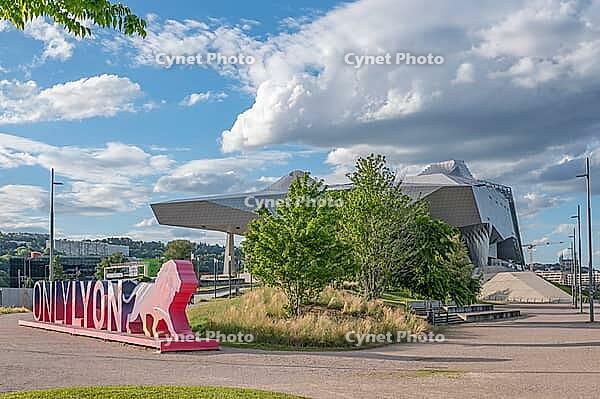 Colourful OnlyLyon marketing sculpture with lion figure as the city's landmark against the futuristic backdrop of the Musee des Confluences by Coop Himmelblau, surrounded by green trees and white clouds in the blue sky in Lyon La Confluence, Rhone, Auverg [IBR125002339]