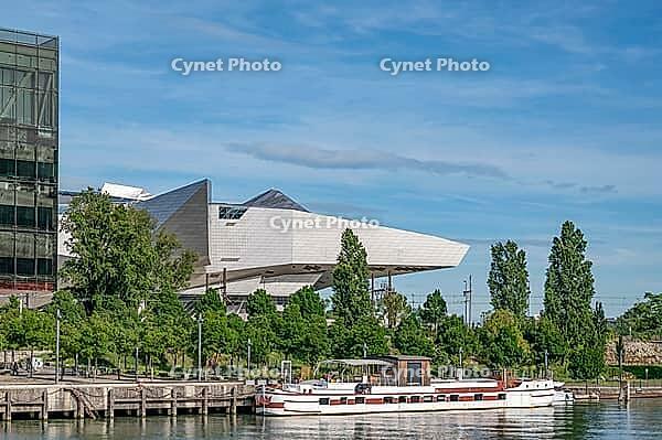 The deconstructivist architecture of the Musée des Confluences, designed by the Viennese architectural firm Coop Himmelb (l) au, on the banks of the Saône at Quai Rambaud, with a traditional péniche moored by the river against a backdrop of green trees, s [IBR125002342]