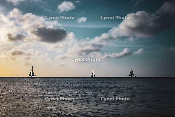Three sailboats on a calm sea with a dramatic sky filled with clouds during sunset. Aruba, The Netherlands [IBR125026134]
