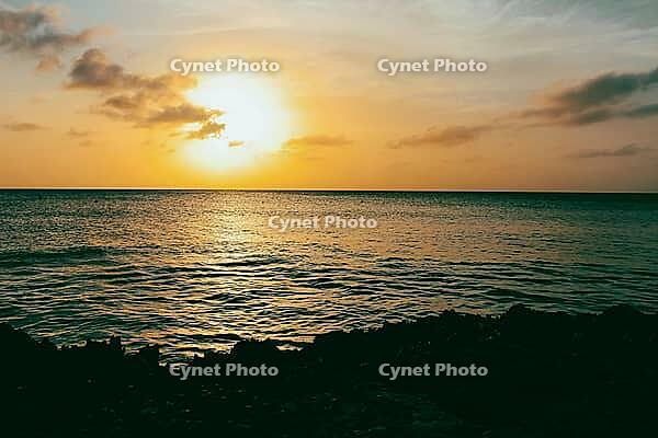 A tranquil sunset over a calm ocean, with orange and yellow hues reflecting on the water, aruba [IBR125026141]