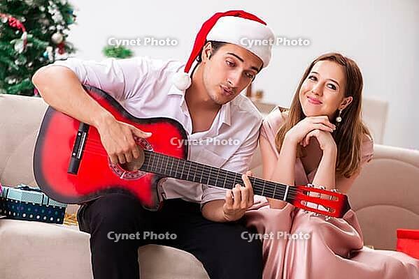 Young couple playing guitar at christmas [IBR125053257]
