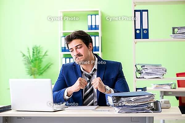 Businessman unhappy with excessive work sitting in the office [IBR125062190]