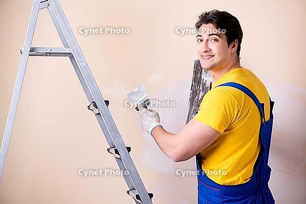 Young contractor employee applying plaster on wall [IBR125062249]