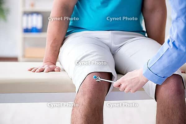Doctor checking nerve reflexes with hammer [IBR125094353]