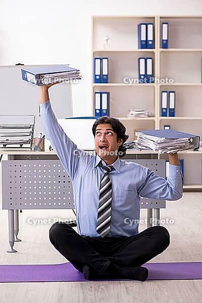 Young handsome male employee doing exercises in the office [IBR125117995]