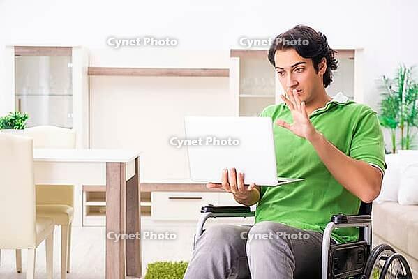 Young handsome man in wheelchair at home [IBR125117997]